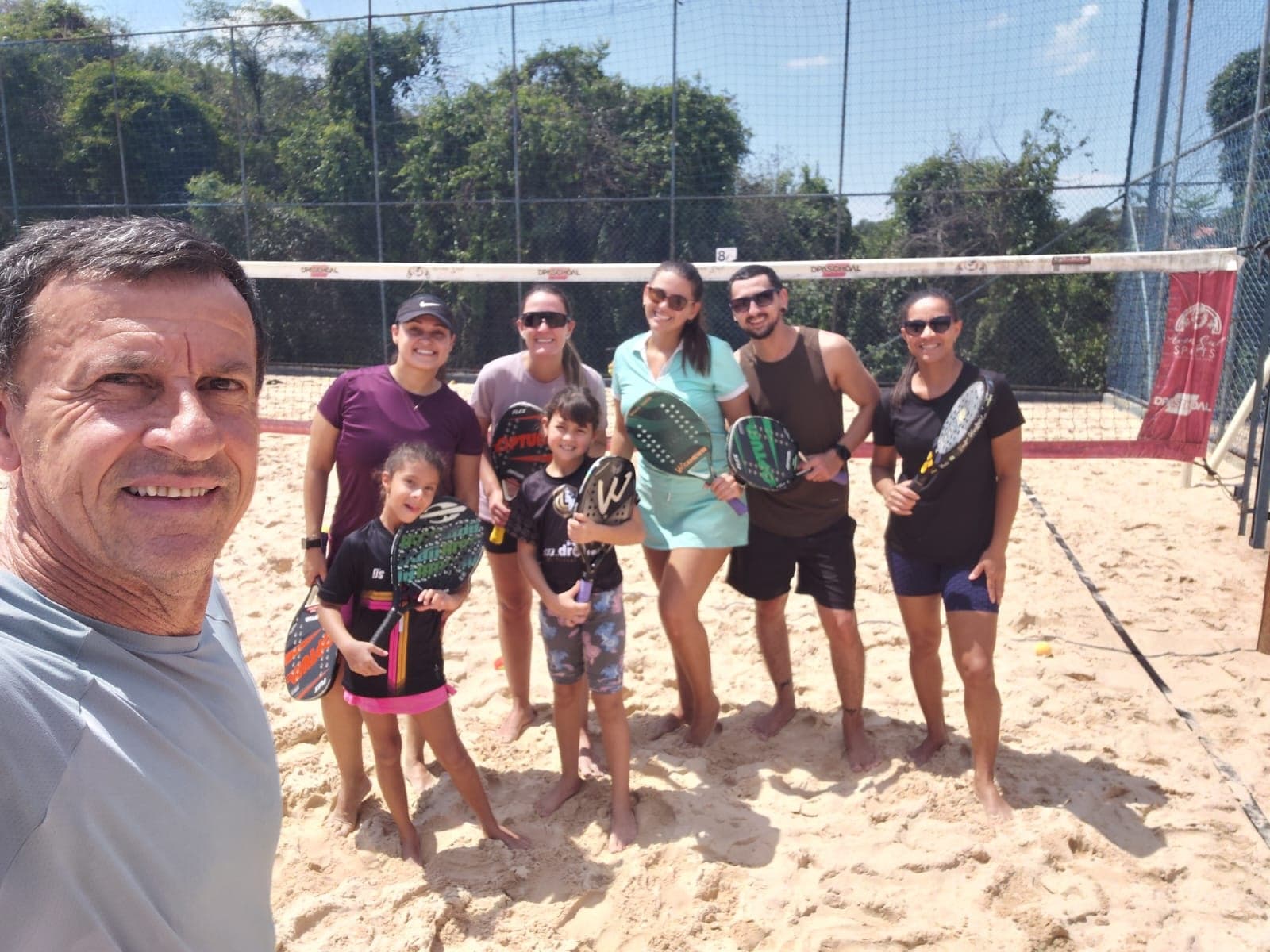 Turma com raquetes na quadra de Beach Tennis da Arena Sul durante o dia.
