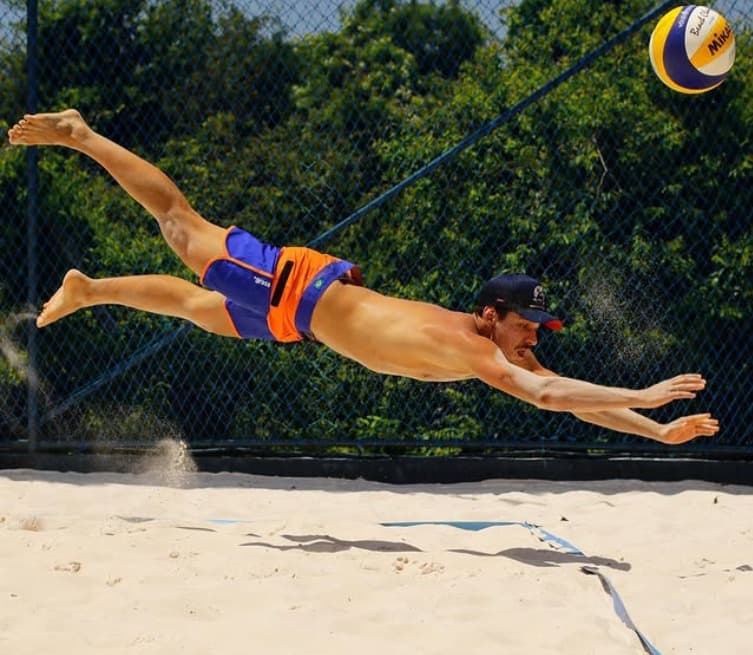 Jogador mergulha para alcançar a bola durante uma partida de vôlei de praia.